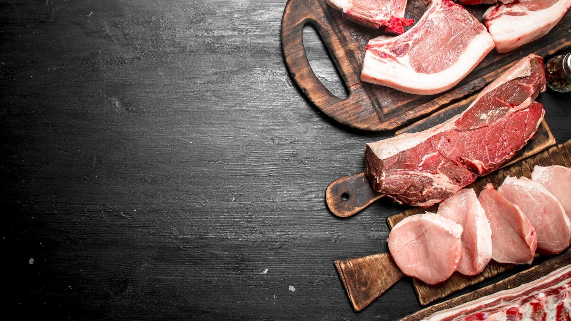 Rohes Fleisch auf Holzbrettern vor dunklem Hintergrund